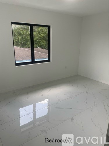 A bedroom with a large window and marble flooring is available for rent.