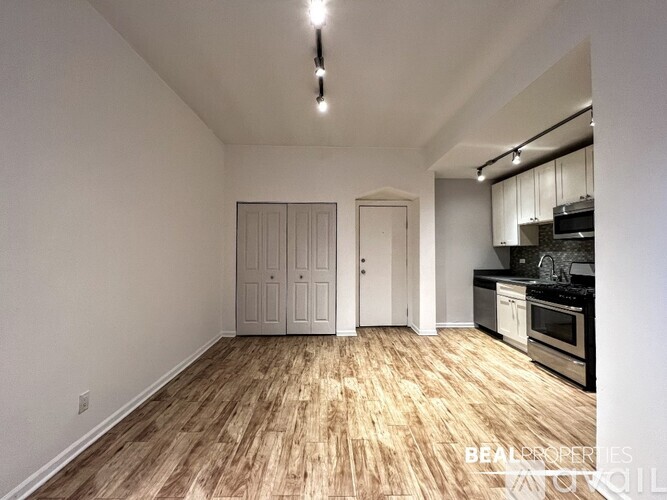 A room with wooden flooring and a kitchen area in the background.