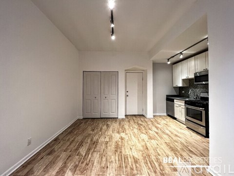 A room with wooden flooring and a kitchen area in the background.