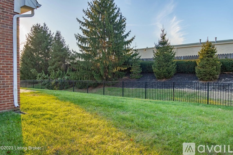 A grassy area with a fence and trees in front of a building.
