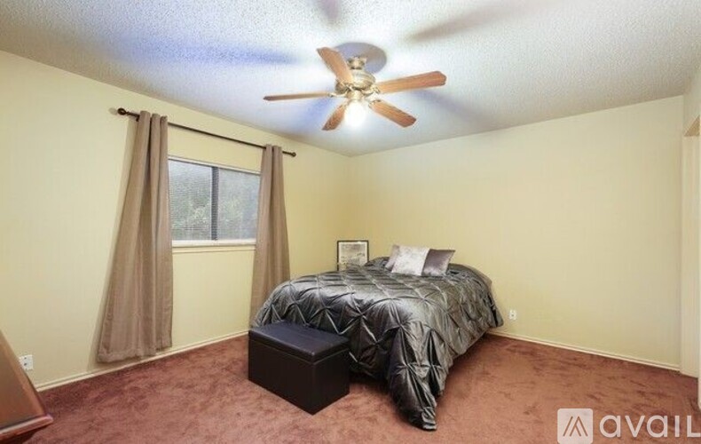 A bedroom with a bed, a ceiling fan, and a window with curtains.