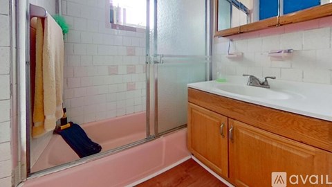A bathroom with a pink tub and wooden cabinets.