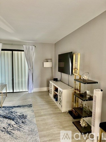 A modern living room with a television, a glass coffee table, and a blue rug.