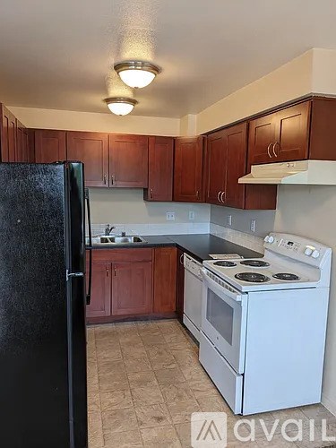 A kitchen with a black refrigerator, white stove, and brown cabinets.