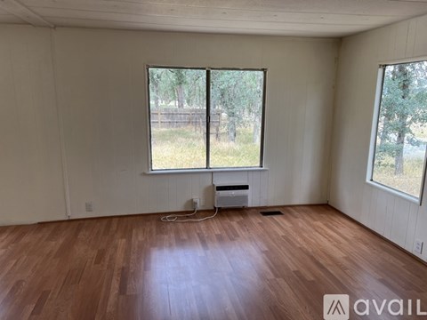 A room with wooden floors and two windows overlooking a fence.