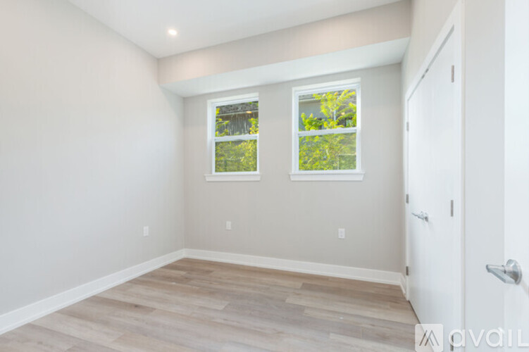 A room with a white door and two windows with a view of trees.