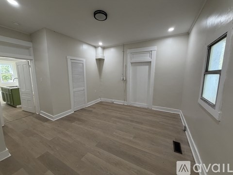 A room with white walls and wooden flooring, with a window on the right side.