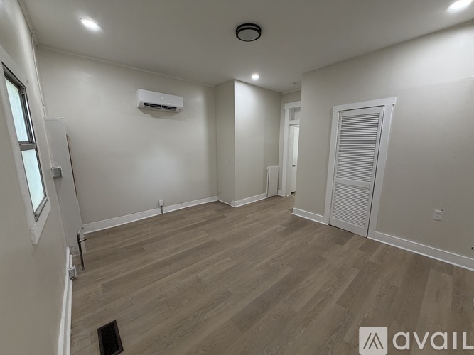 A room with a wooden floor and a white wall with a window and a door.