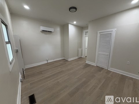 A room with a wooden floor and a white wall with a window and a door.
