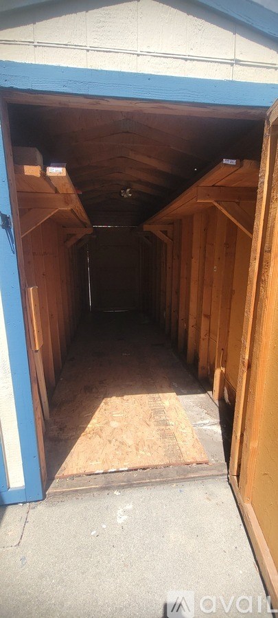 A long, narrow storage space with wooden walls and a blue door at the end.