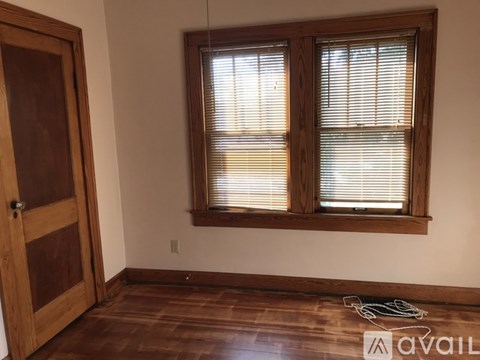 A room with a wooden floor, a door, and a window with blinds.