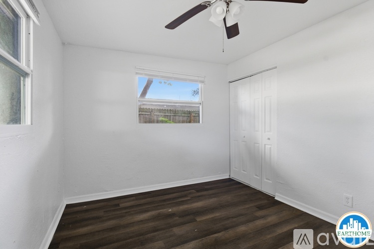 A room with a ceiling fan and a window with a view of a fence and trees outside.