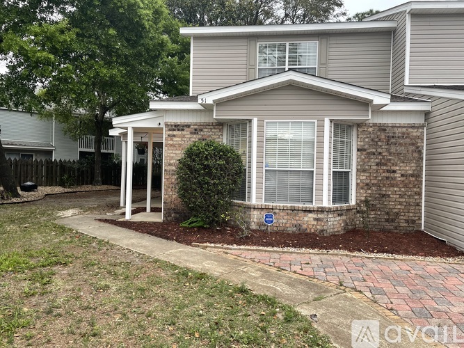 A house with a grey siding and a brick wall with a bush in front.