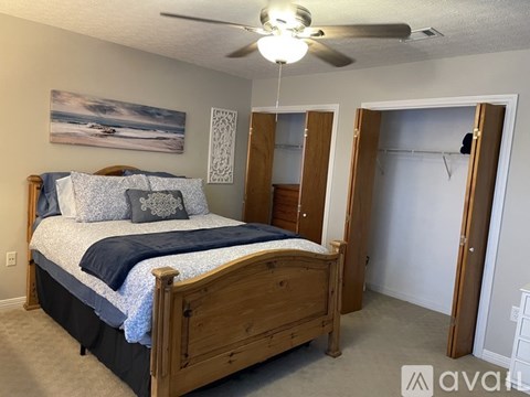 A bedroom with a bed, a ceiling fan, and a painting on the wall.