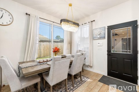 A dining room with a table set for four and a view of a fence and trees outside the window.