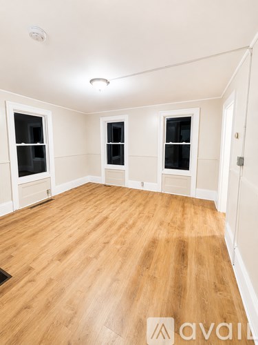 A room with wooden flooring and three windows.
