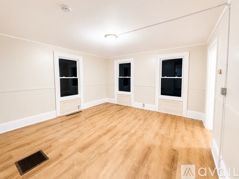 A room with wooden flooring and three windows.