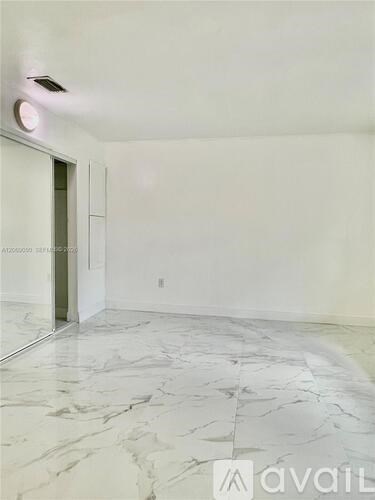 A spacious room with marble flooring and a door on the left.