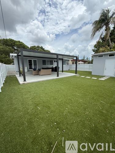 A house with a grey roof and a white fence is surrounded by a green lawn.
