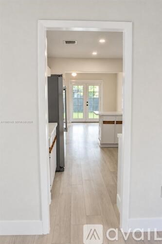 A white hallway with a refrigerator on the left and a kitchen in the distance.