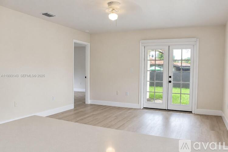 A room with a door and a window with a view of a fence and trees.