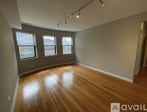 A room with wooden flooring and three windows.