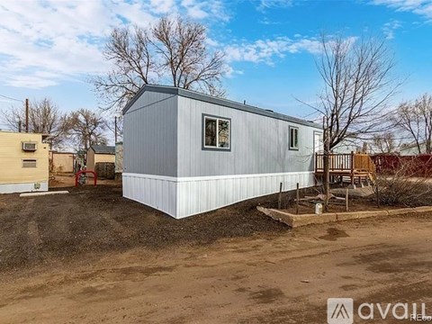 A small house with a grey exterior is situated in a dirt lot.