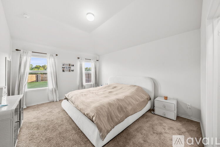 A bedroom with a large bed and a window with curtains.