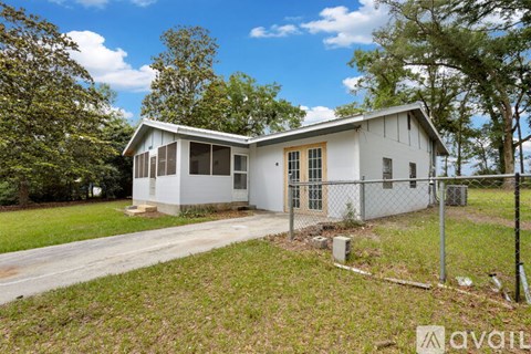 A house with a white exterior and a grey roof is surrounded by a grassy area and trees.