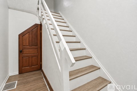 A wooden staircase with a white railing and a brown door.