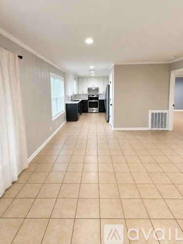 A spacious room with beige tiled flooring and a kitchen area in the background.