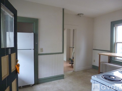 A room with a white wall and a white fridge.