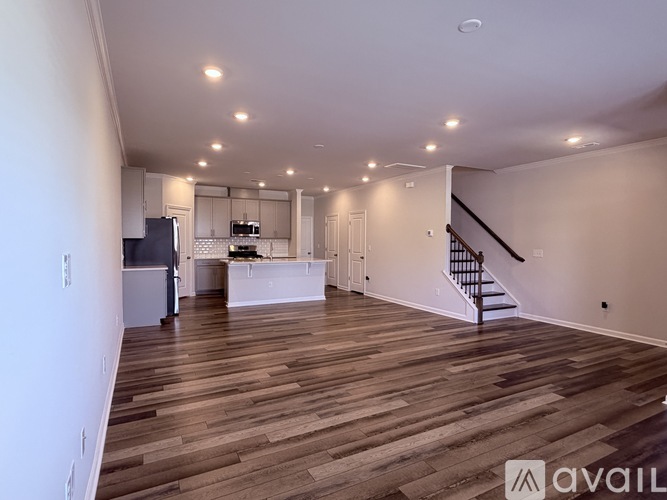 A spacious room with wooden flooring and a staircase on the right side.