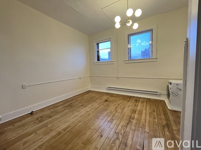 A room with wooden flooring and two windows.