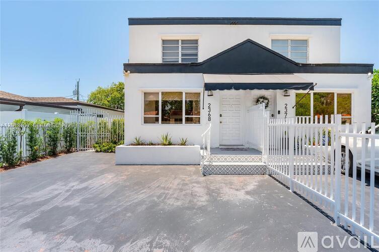 A white house with a black roof and a white picket fence.