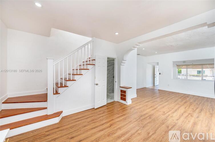 A spacious room with wooden floors and a staircase leading to the upper level.