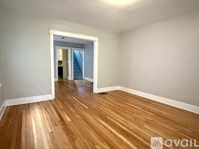 A room with wooden flooring and a white wall with a doorway leading to another room.
