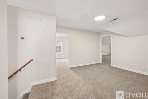 A spacious room with a carpeted floor and a staircase on the left side.