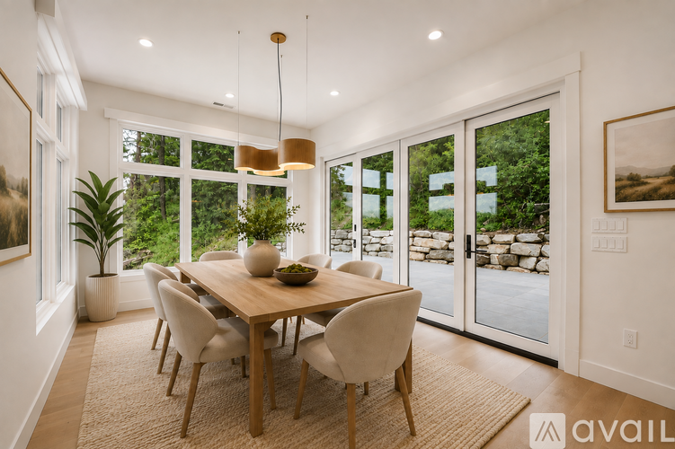 A dining room with a table set for six and a view of a stone wall and trees outside.