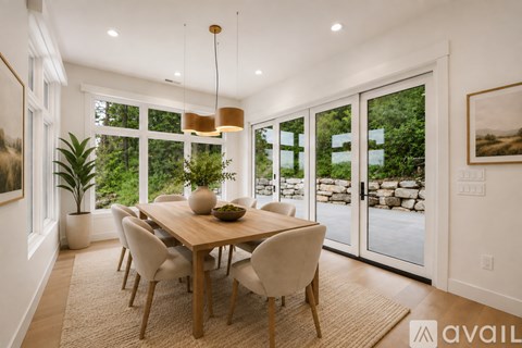 A dining room with a table set for six and a view of a stone wall and trees outside.