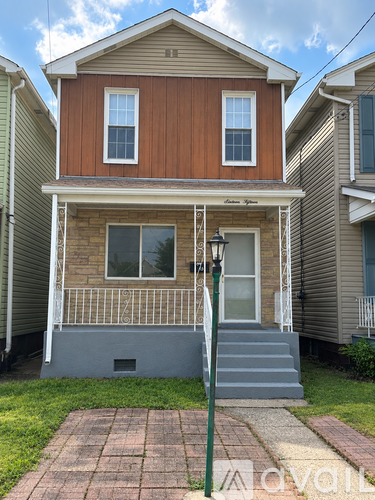A brown and beige house with a porch and a brick walkway.