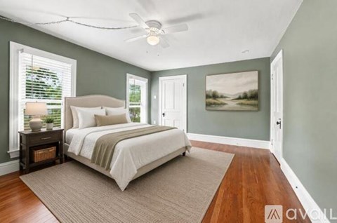 A bedroom with a bed, a ceiling fan, and a painting on the wall.