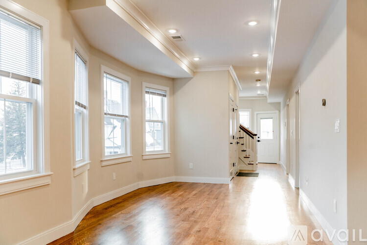 A spacious room with wooden floors and a staircase in the background.