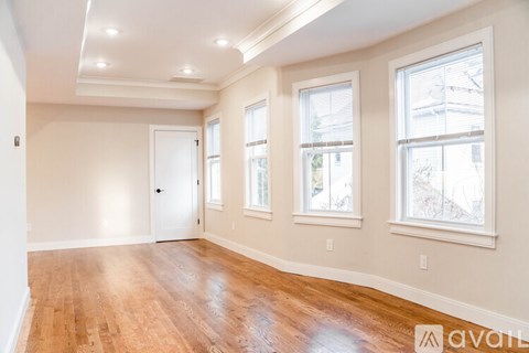 A spacious room with wooden floors and three windows.