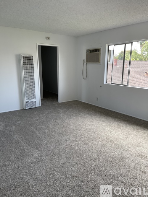 A room with a carpeted floor, a window with blinds, a door, and a wall-mounted phone.