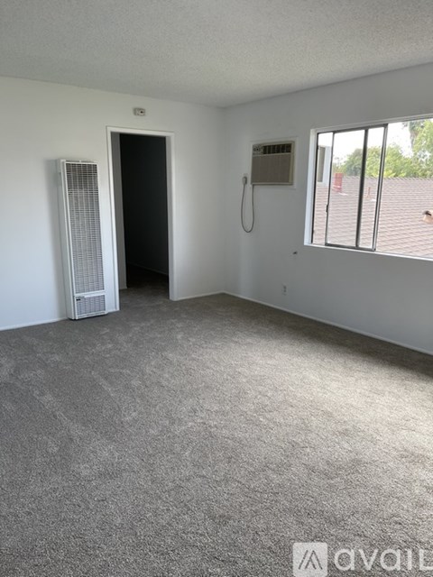 A room with a carpeted floor, a window with blinds, a door, and a wall-mounted phone.