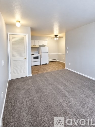 A carpeted room with a white door leading to a kitchen.