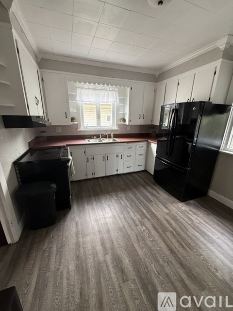 A kitchen with a black fridge and wooden flooring.