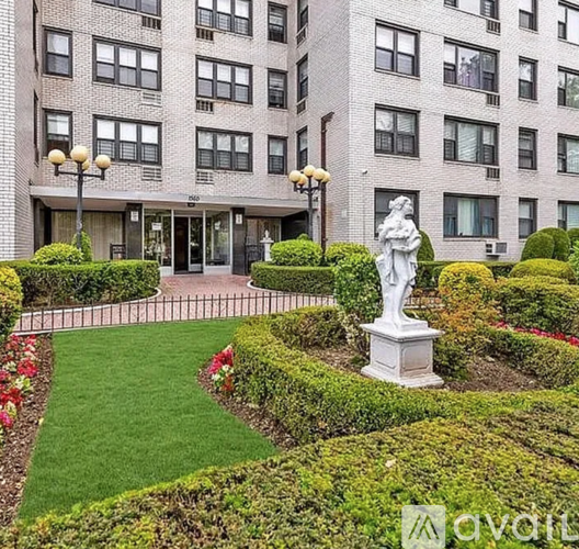 A statue of a woman holding a child is in the middle of a garden with a building in the background.