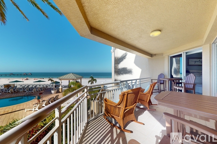 A balcony with chairs and a table overlooking a pool and beach.
